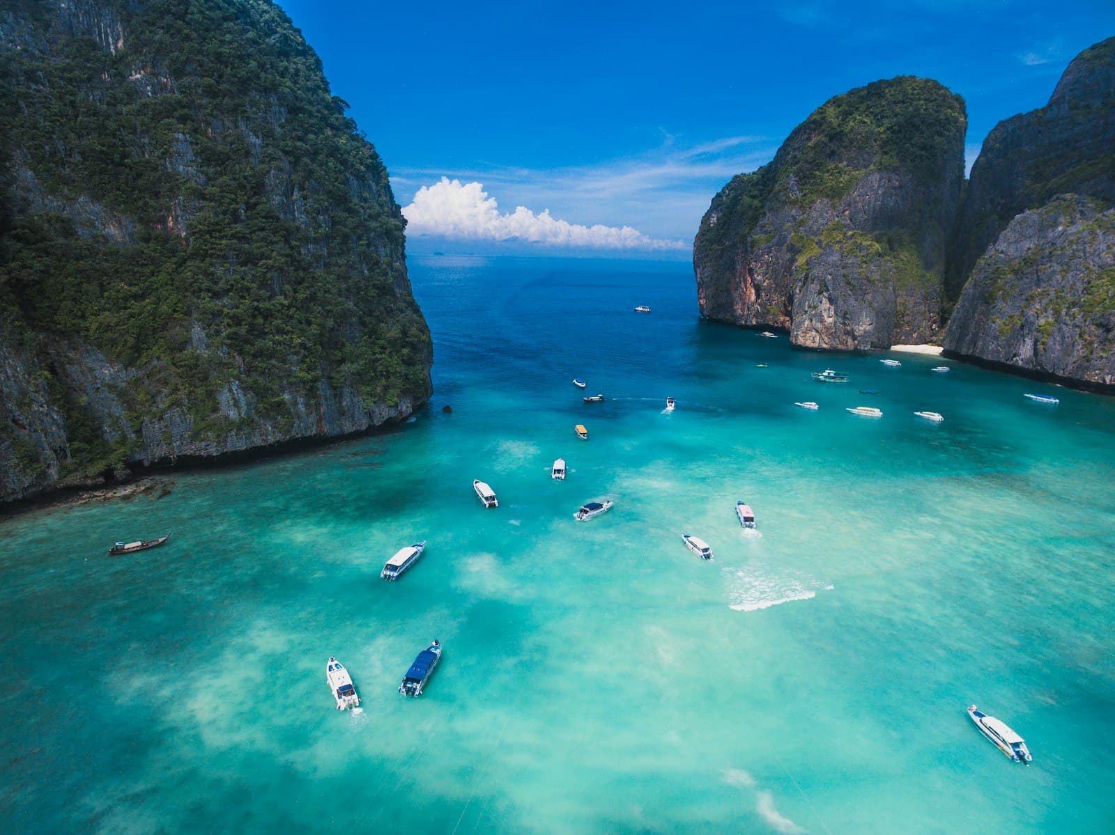 Boats in a turquoise bay below limestone cliffs, Thailand