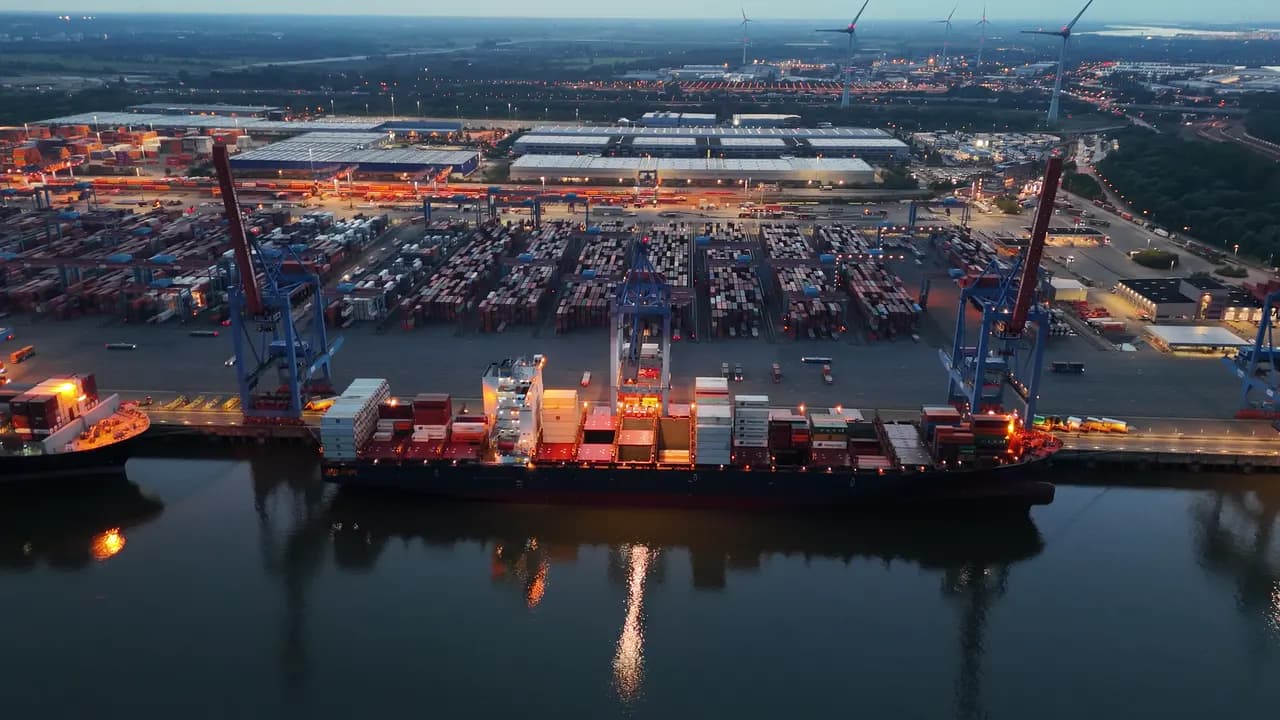 Aerial view at dusk of a container ship under gantry cranes at a lit terminal
